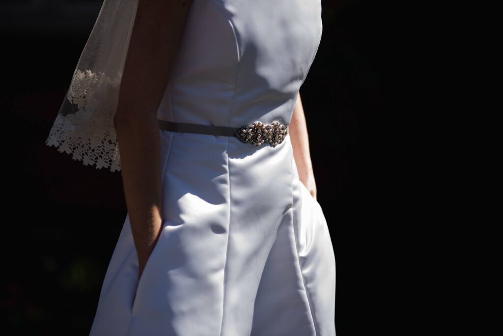 Detail photo of Amy wearing her wedding dress; her face is not showing and her hands are in the pockets. The bottom of her veil is visible.