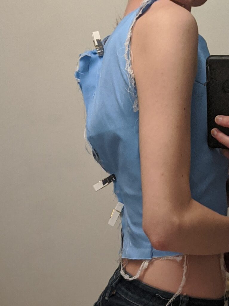 A closeup from the side of Amy's torso showing the fit of the blue mock-up of her wedding dress bodice. It is held together by clothespins because it is too small.