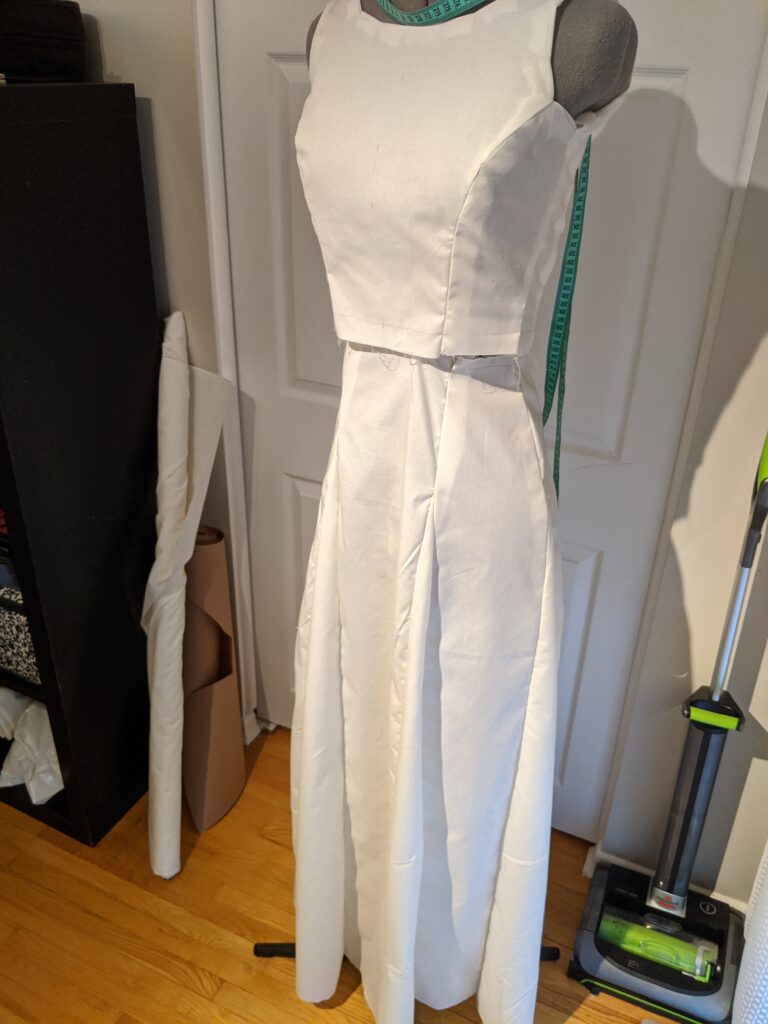 Image of a bodice and separate skirt on a dress form. The skirt is made up of relatively narrow panels connected by triangular godets, and reaches the floor.