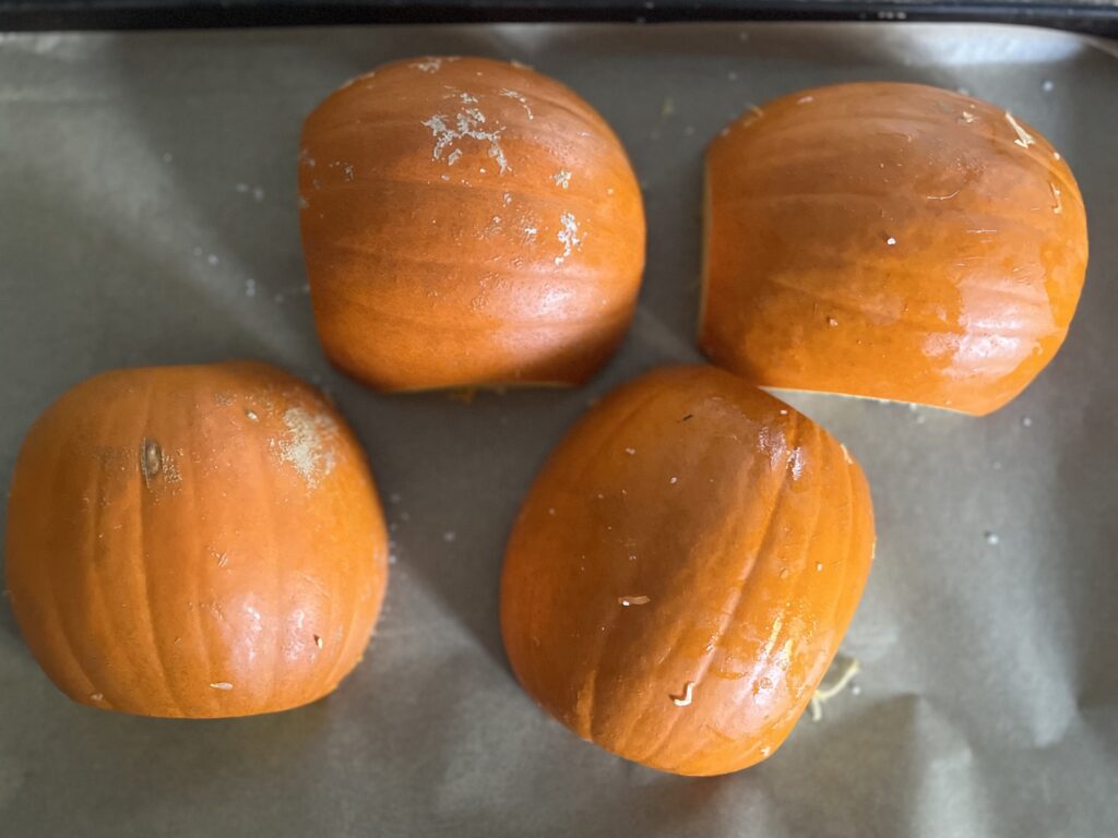 Two pie pumpkins, sliced in half and face down on a baking sheet