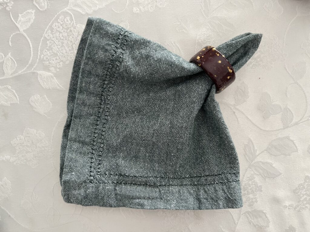 A green napkin has been partly fed through a brown napkin ring.
