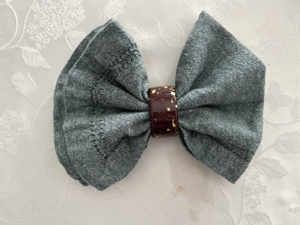 A green napkin has been partly fed through a brown napkin ring and shaped into a bow.