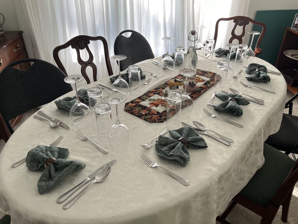 An oval table with a white table cloth is set for eight guests, including the napkin bows described in this blog post