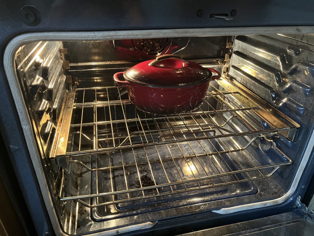 A dutch oven in the centre of an oven, with its lid on.