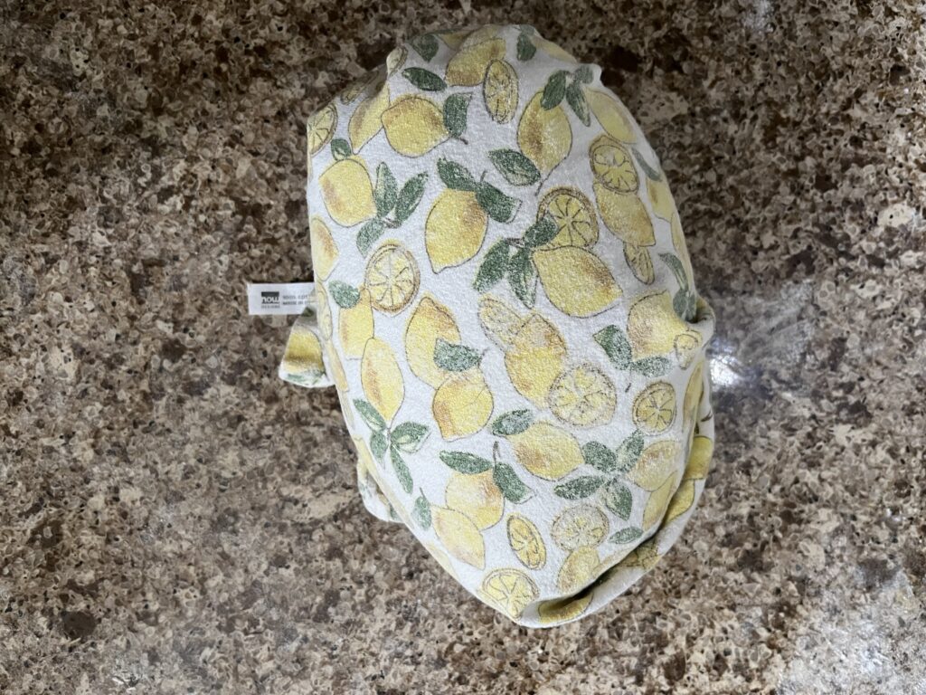 A loaf of bread dough is tightly wrapped in a tea towel, sitting on a counter.