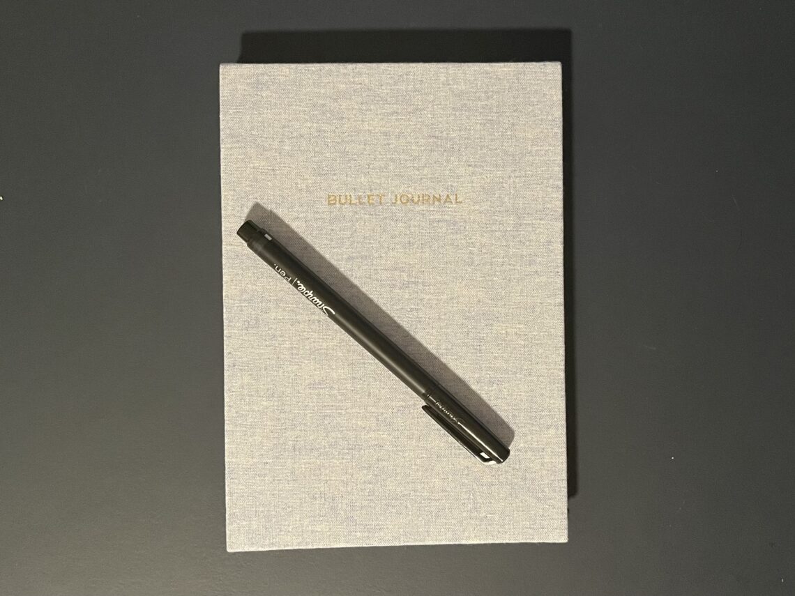 A closed notebook labeled "Bullet Journal" with a felt tip pen sitting on top.