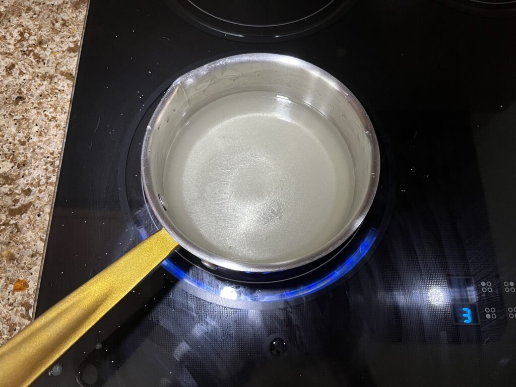 A pot on the stove containing water and nearly dissolved sugar