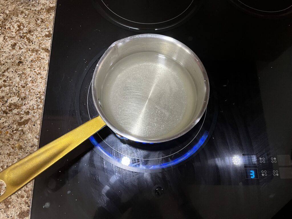 A pot on the stove containing water and sugar that is barely perceptible but not quite fully dissolved