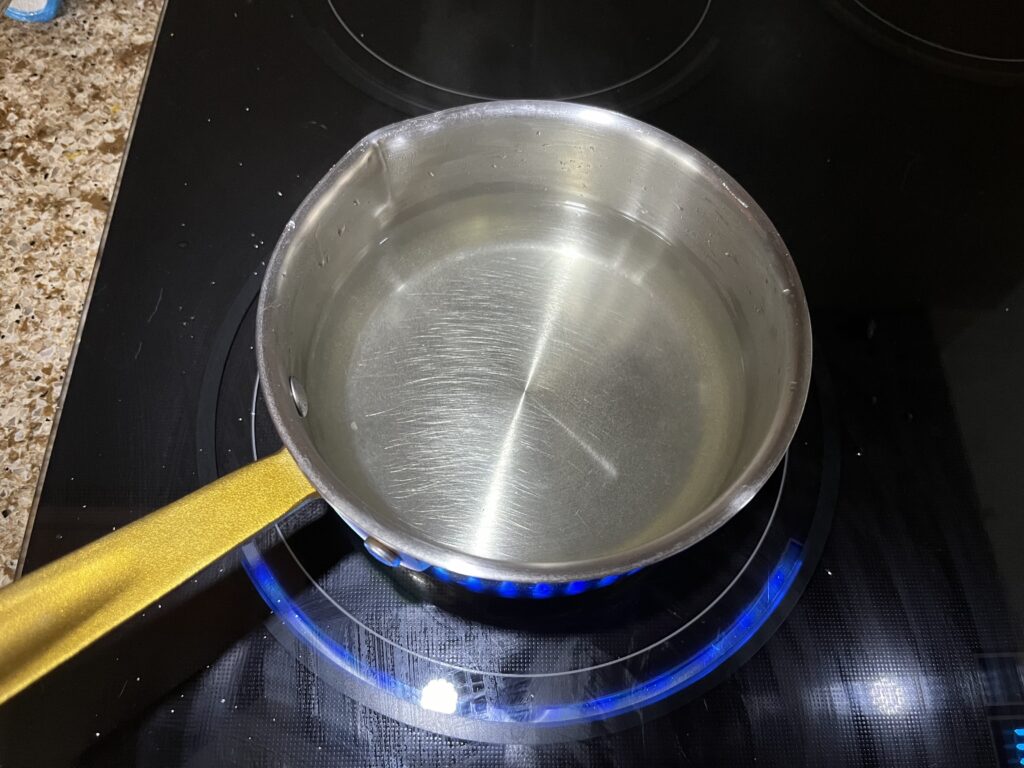 A pot on the stove that appears to contain only water but is slightly yellow due to the dissolved sugar