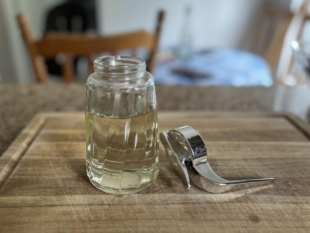 An open syrup jar nearly full of syrup, with its lid next to it