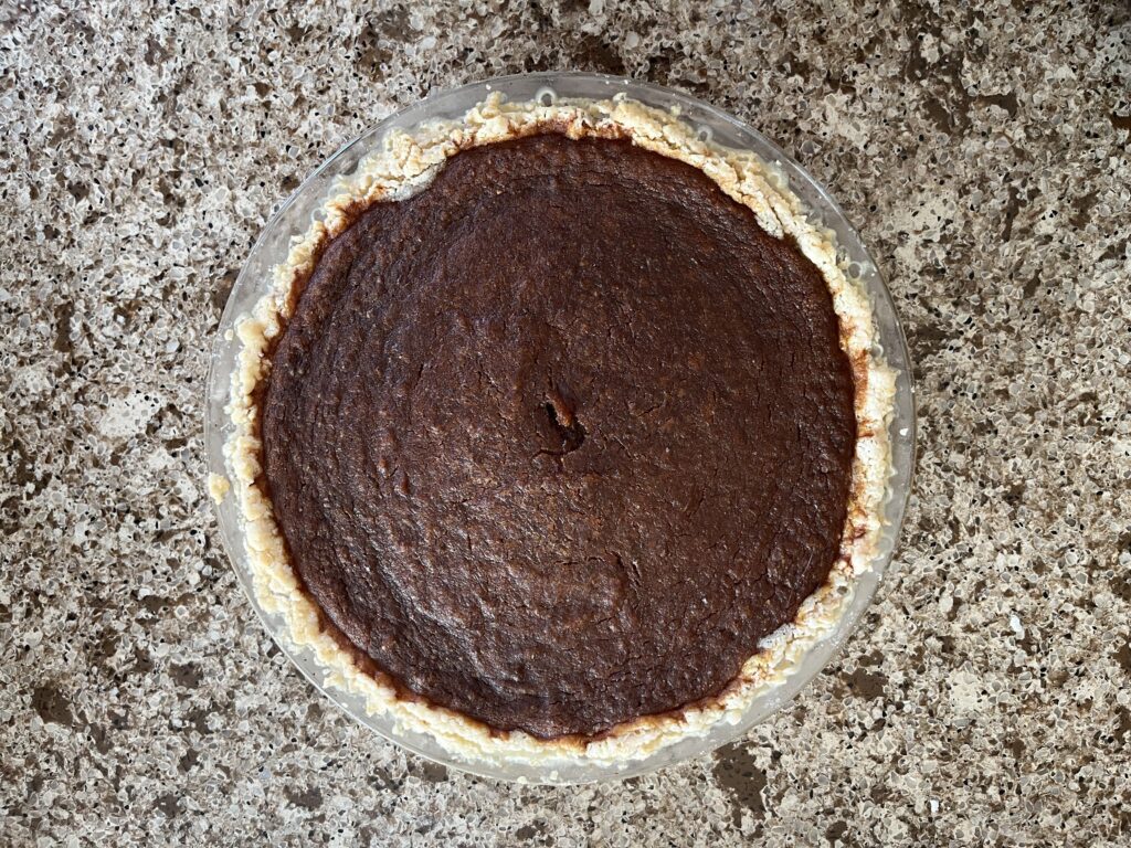 Close-up of a baked vegan pumpkin pie. It is the colour of burnt toffee (deep brown).