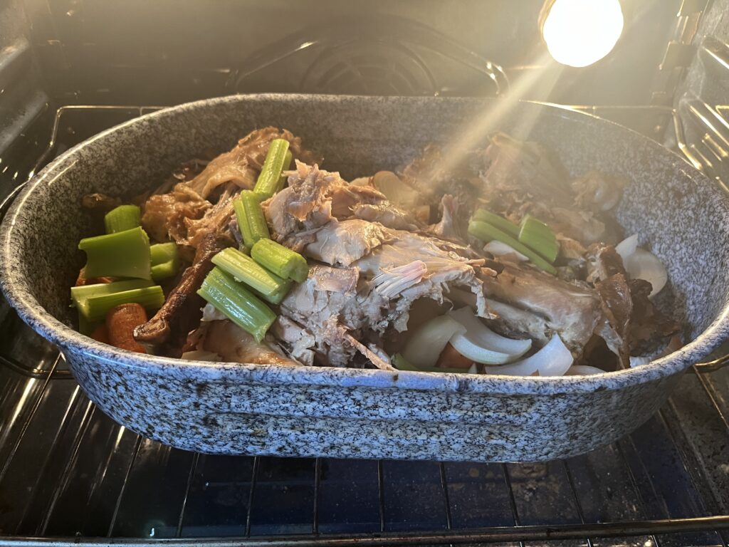 A large roasting pan sits in an oven. It is full of turkey bones and vegetables.