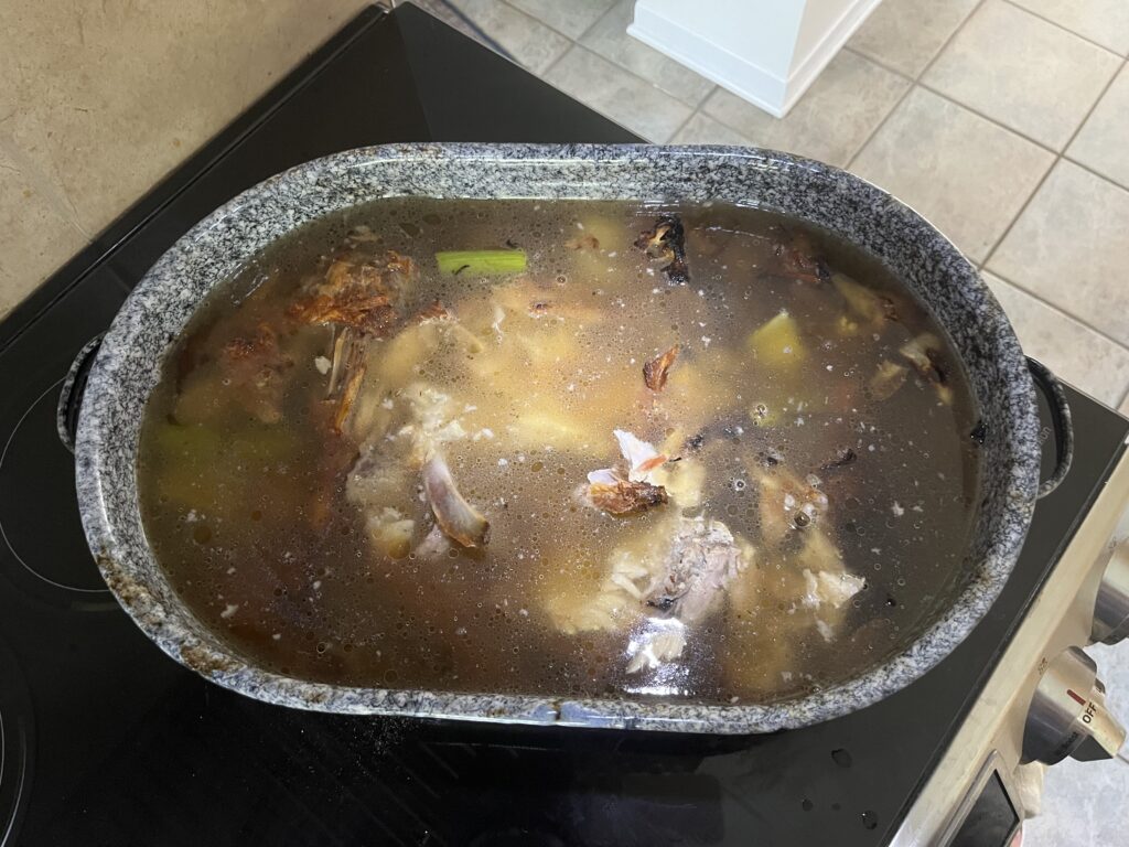 A large roasting pan is filled with liquid, through which pieces of vegetables and turkey bones are visible.