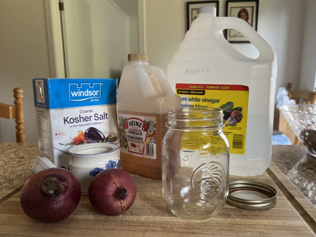 Most of the ingredients for pickled red onions sit on a cutting board next to an empty mason jar.