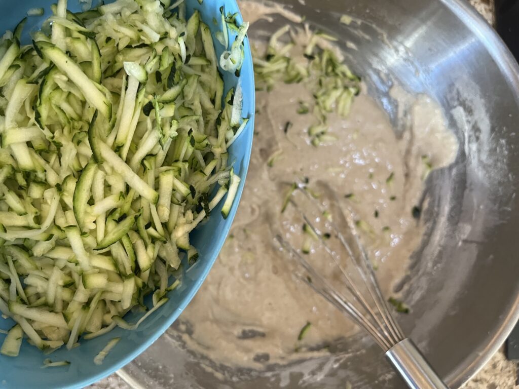 A close-up of shredded zucchini, with muffin batter in the background