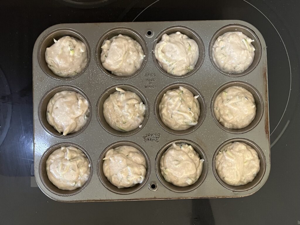 Uncooked muffin batter spooned into a muffin tin.