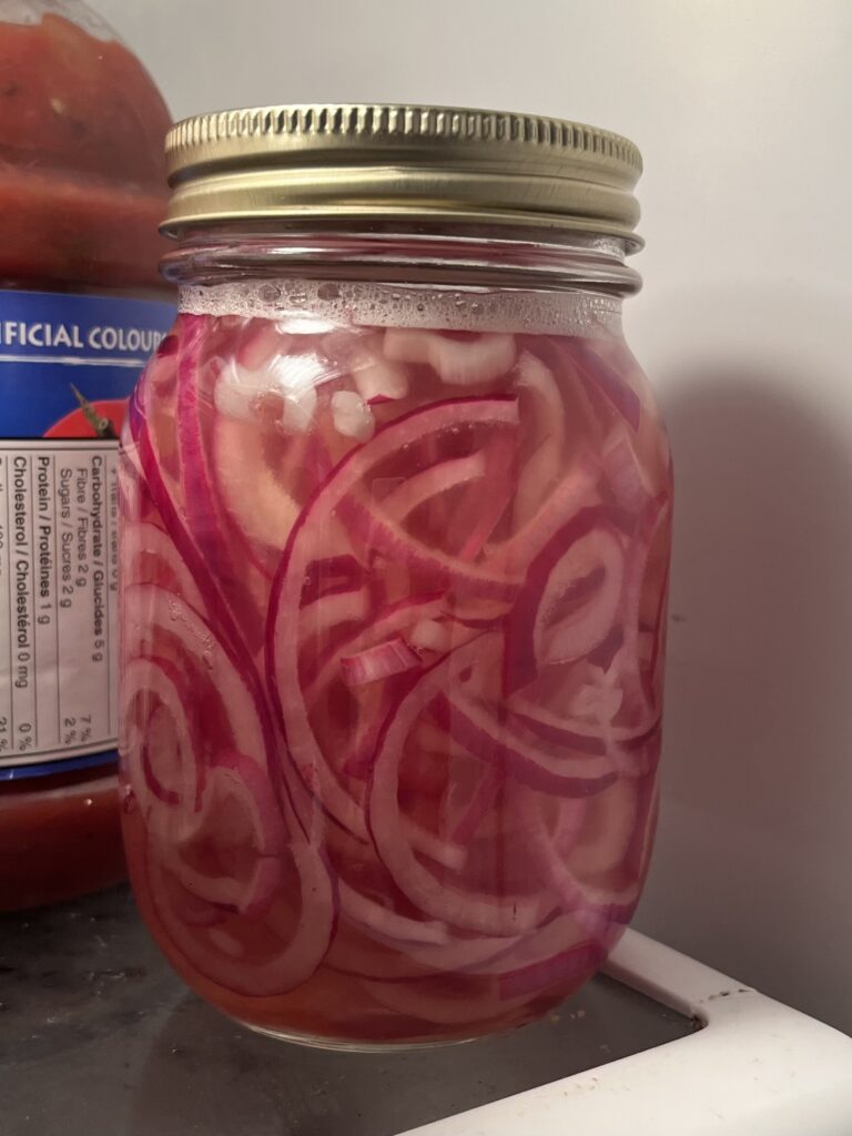 A close up of a jar of pickled red onions. The liquid is a little pink.