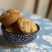 Three zucchini muffins sit in a bowl on top of a blue and white table cloth