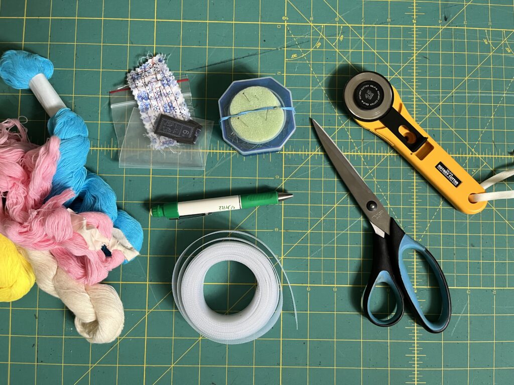 Close-up of a self-healing cutting mat covered with various sewing tools mentioned in this post, including Japanese basting thread and needles, horsehair braid, silk pins, and so on