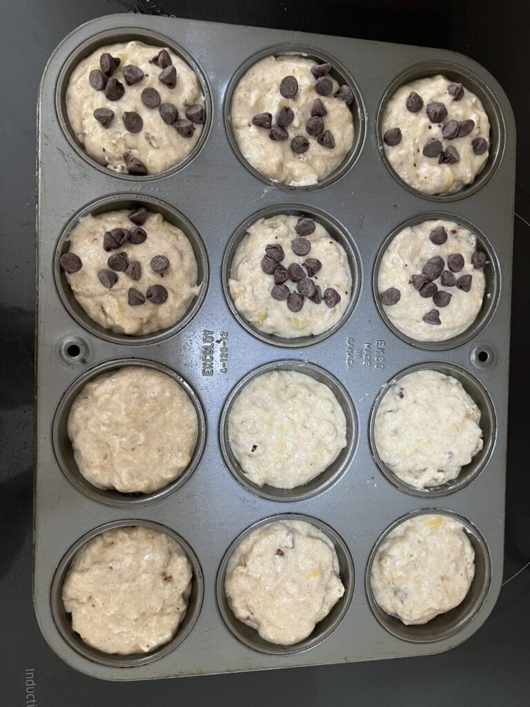 Muffin tin filled with batter before baking. Half have chocolate chips on top.