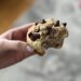 Close-up of a banana muffin with chocolate chips on top. It's held in a hand and a bite has been taken out.