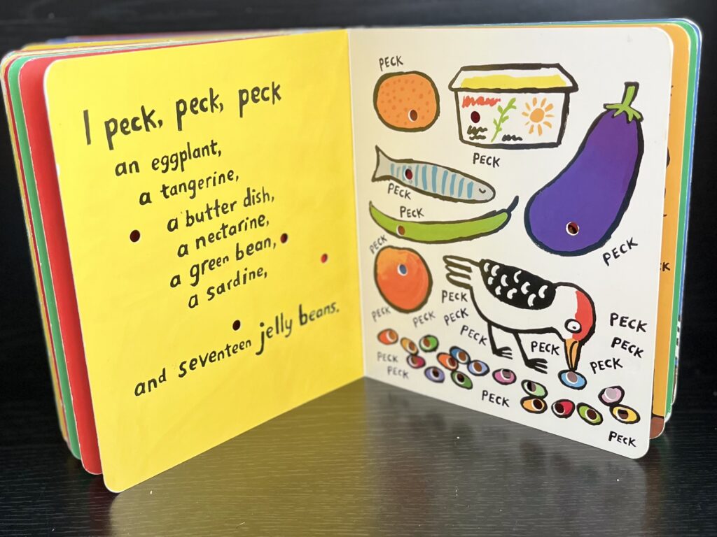 Close-up of inside pages from the board book Peck, Peck, Peck. There are small holes punched out of the book, showing where the baby woodpecker character has pecked the various foods depicted on the page.